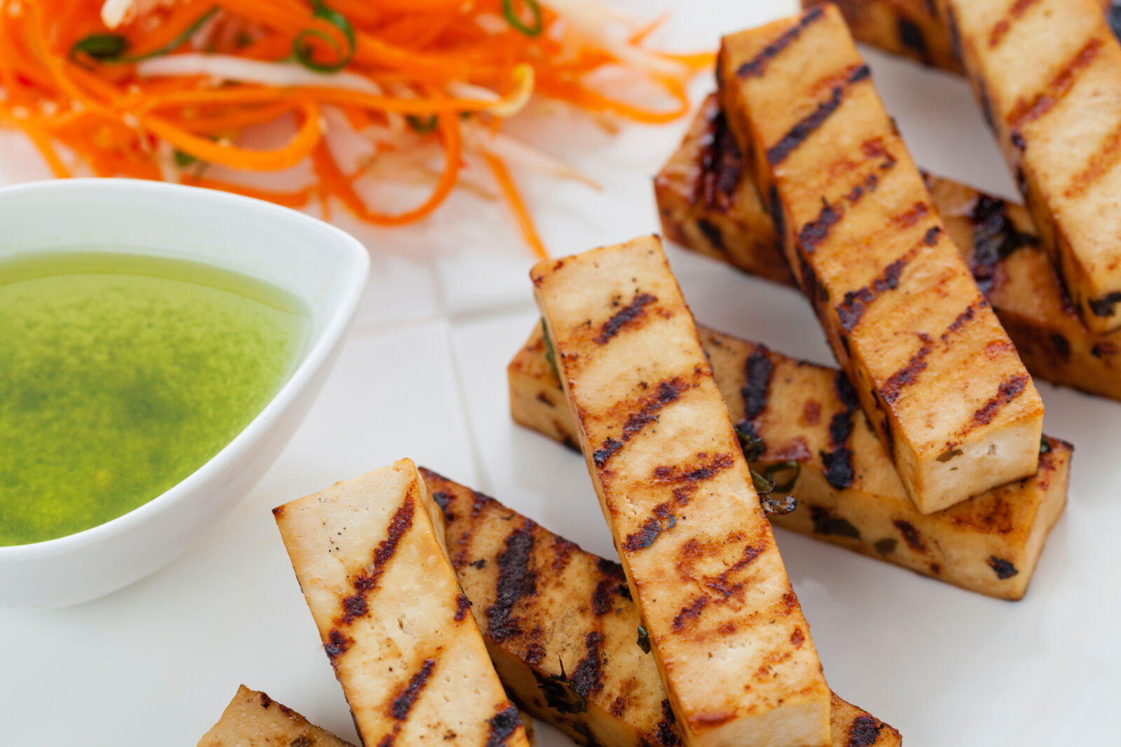 Grilled tofu on sticks next to dipping sauce.