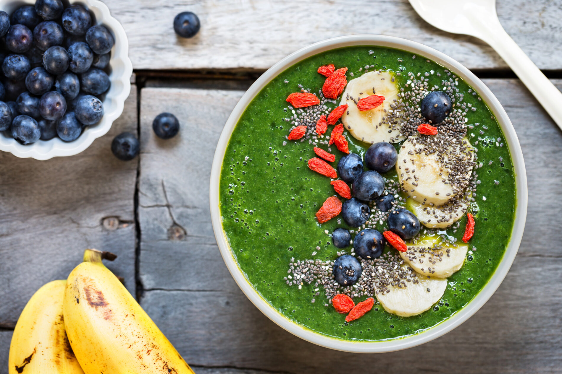 Green smoothie bowl topped with bananas, goji berries, blueberries, and chia seeds.