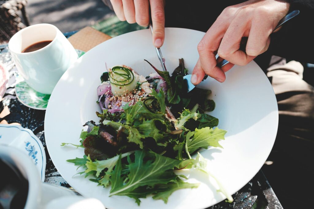 Person eating a salad at a table with coffee.