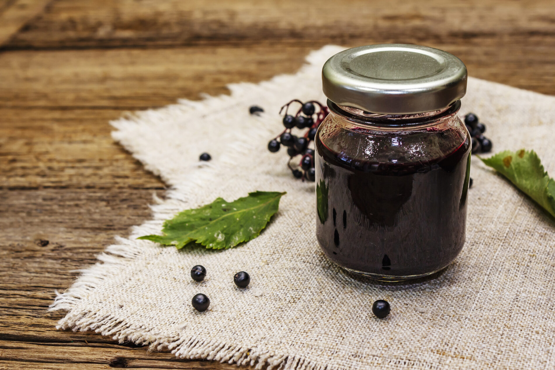 Elderberry syrup in a glass jar with some elderberries on the table nearby.